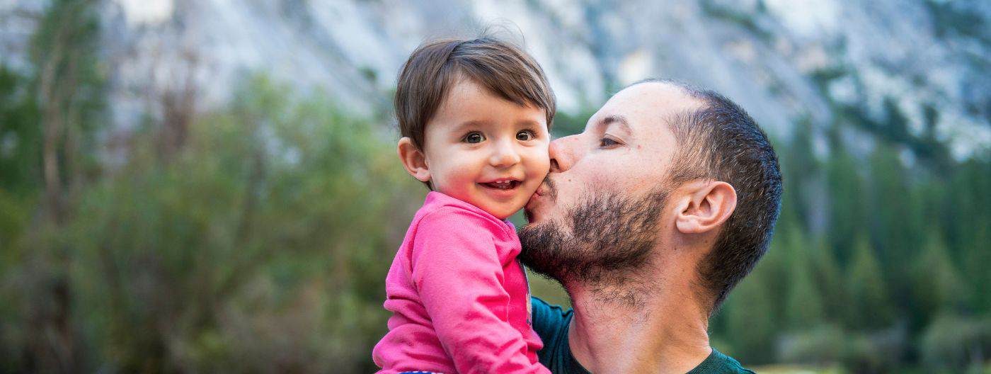 Father kissing a child, with mountains in the distance at Yosemite National Park.