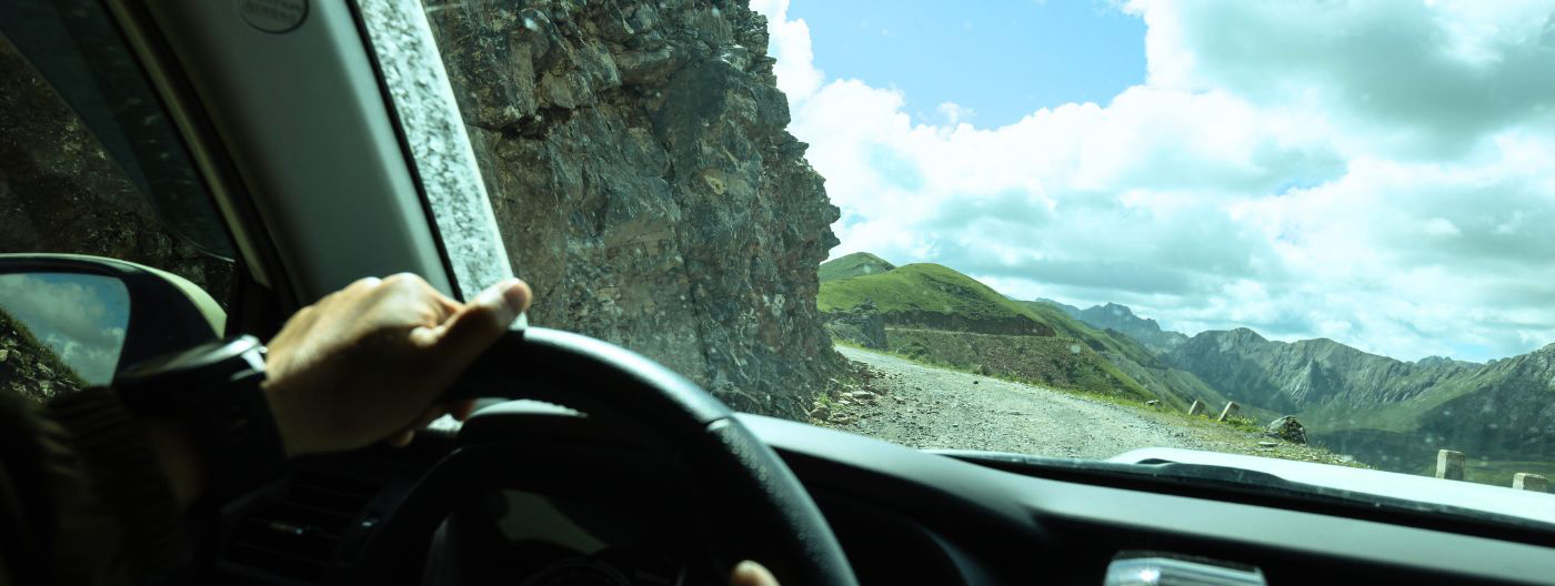 Person with hands on the wheel of a car as it navigates a turn on a gravely road high in the mountains