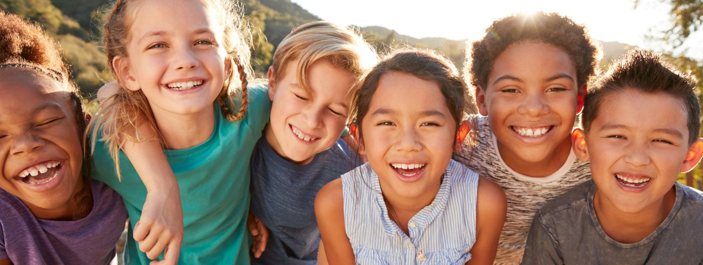 Children smiling with their arms on each other's shoulders, with mountains in the background.